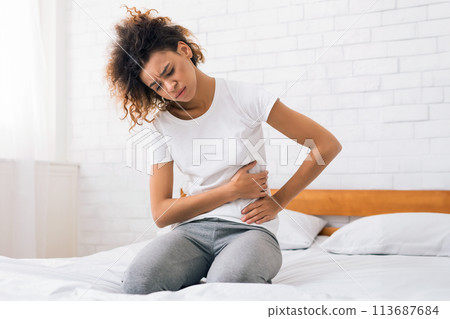 African-american girl suffering from abdominal pain on bed African-american girl suffering from abdominal pain on bed 113687684