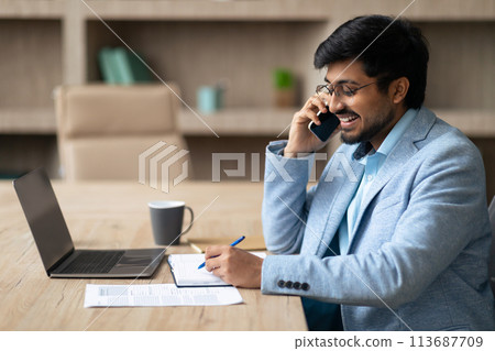 Middle Eastern businessman managing calls writing notes at office laptop 113687709