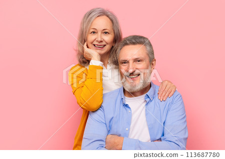 Smiling senior couple hugging posing for portrait against pink backdrop 113687780