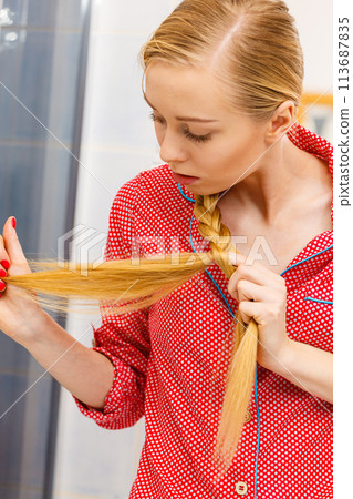 Blonde woman looking at her hair ends Blonde woman looking at her hair ends 113687835