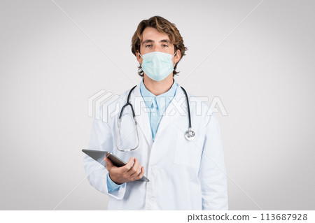 Serious male doctor with mask holding digital tablet 113687928