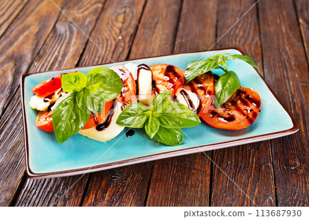 Italian caprese salad with sliced tomatoes, mozzarella, basil, olive oil on wooden background. Top view. Italian caprese salad with sliced tomatoes, mozzarella, basil, olive oil on wooden background. Top view. 113687930