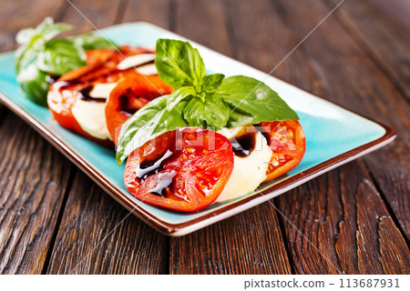 Italian caprese salad with sliced tomatoes, mozzarella, basil, olive oil on wooden background. Top view. Italian caprese salad with sliced tomatoes, mozzarella, basil, olive oil on wooden background. Top view. 113687931