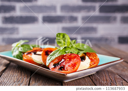 Italian caprese salad with sliced tomatoes, mozzarella, basil, olive oil on wooden background. Top view. Italian caprese salad with sliced tomatoes, mozzarella, basil, olive oil on wooden background. Top view. 113687933
