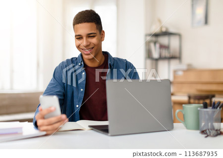 Man smiling at phone with laptop on desk Man smiling at phone with laptop on desk 113687935