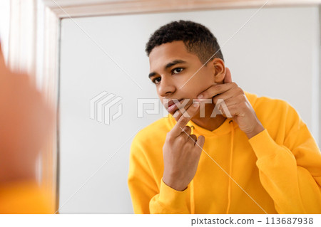 Teen guy examines acne in the mirror, skin health 113687938