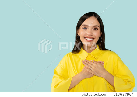 Cheerful happy thankful hispanic young casual woman holding hands on chest and smiling at camera 113687964