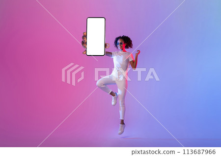 Energetic black woman jumping with blank smartphone screen on neon background 113687966