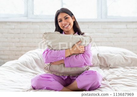 Woman hugging pillow and smiling on bed 113687969