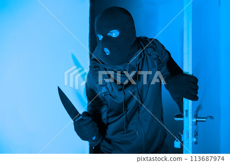 Armed burglar sneaking into a room at night 113687974