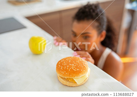 woman battles temptation at kitchen choosing between apple and cheeseburger 113688027