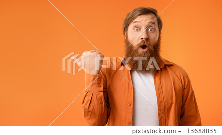 Surprised redhaired man with beard pointing thumb finger aside, studio Surprised redhaired man with beard pointing thumb finger aside, studio 113688035