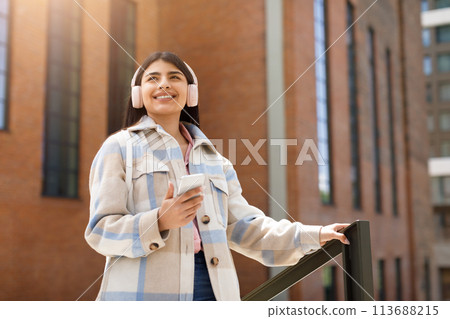 Happy girl listening to music on city street 113688215