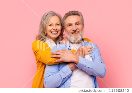Loving retired mature couple embraces posing together against pink background Loving retired mature couple embraces posing together against pink background 113688240