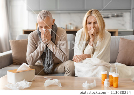 Sick couple blowing noses on couch 113688254
