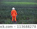 Rear view of man wearing orange astronaut space suit standing in green grass outdoors. 113688278
