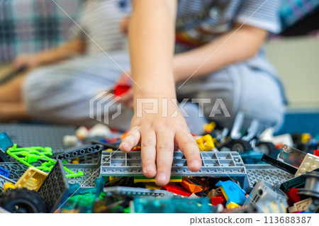 The child reaches out his hand to take the desired piece of the Lego constructor. A child takes a construction piece from a large pile of Legos. Concept child playing with Lego constructor. The child reaches out his hand to take the desired piece of the Lego constructor. A child takes a construction piece from a large pile of Legos. Concept child playing with Lego constructor. 113688387