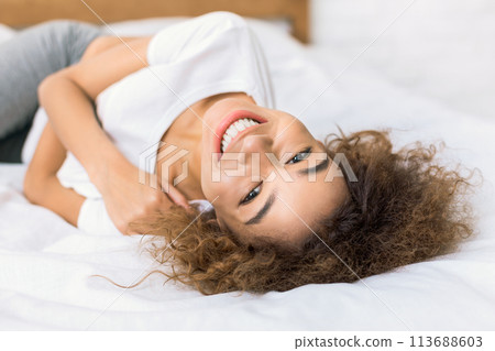 Happy woman lying on bed and looking at camera Happy woman lying on bed and looking at camera 113688603