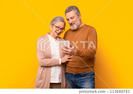 Happy mature gray couple looking at smartphone screen hugging, studio Happy mature gray couple looking at smartphone screen hugging, studio 113688781