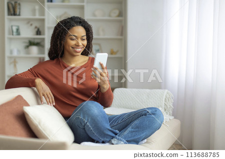 Black Woman Sitting on Couch Using Cell Phone Black Woman Sitting on Couch Using Cell Phone 113688785