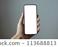 Closeup of woman hand holding smartphone with blank transparent screen for business infographic web site design app. Smartphone screen mockup template on light gray background 113688813
