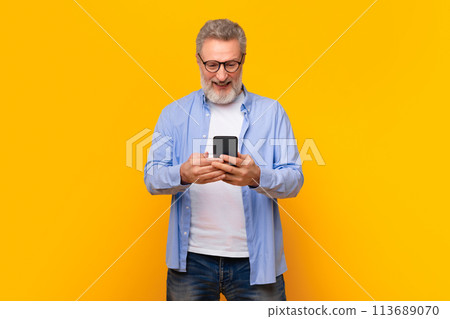 Cheerful mature gray haired man texting via smartphone, yellow background 113689070