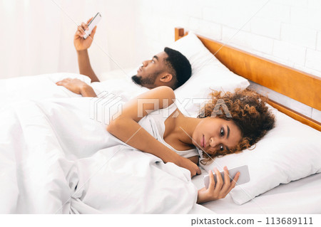 Millennial couple lying on bed back to back with smartphones 113689111