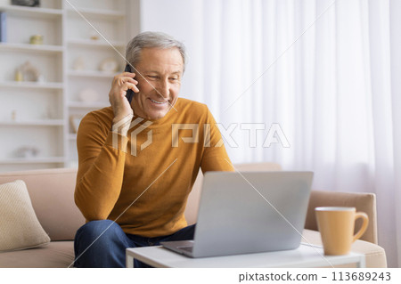 Senior on phone call with laptop in home setting 113689243