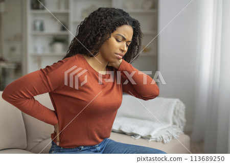 Young Black Woman Experiencing Neck Pain in a Cozy Living Room Young Black Woman Experiencing Neck Pain in a Cozy Living Room 113689250