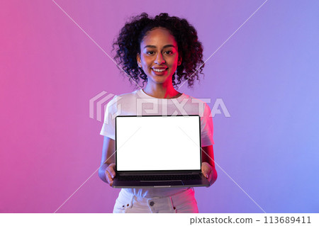Cheerful black woman presenting laptop with blank screen on neon background Cheerful black woman presenting laptop with blank screen on neon background 113689411