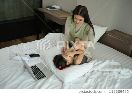 Happy young mother playing with her little daughter on bed while working at home 113689455