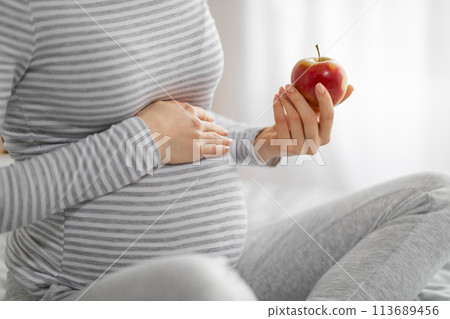 Expectant mother casually holding a red apple 113689456