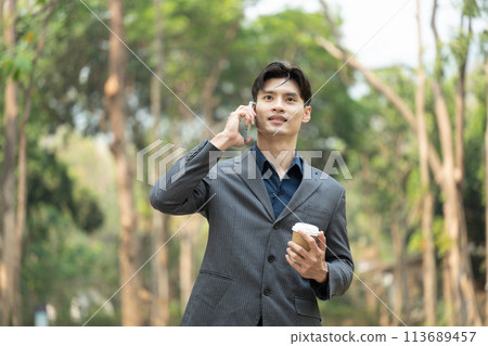 Handsome businessman holding paper cup of coffee and talking on mobile phone at outdoor 113689457