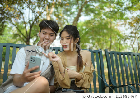 Young couple using mobile phone while sitting on a bench in urban park Young couple using mobile phone while sitting on a bench in urban park 113689467