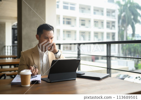 Serious adult businessman wearing suit analyzing financial data on laptop screen Serious adult businessman wearing suit analyzing financial data on laptop screen 113689501