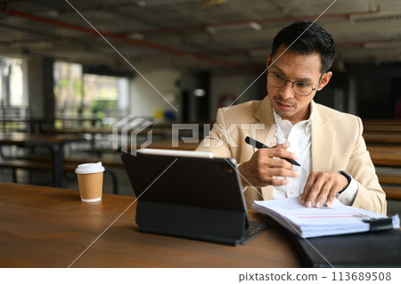 Asian businessman looking at digital tablet and checking financial documents at a cafeteria 113689508
