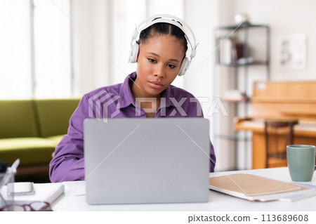 Focused black female student with headphones using laptop 113689608