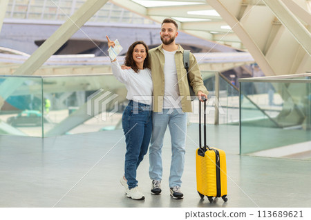 Cheerful Couple Standing With Luggage in Airport Terminal And Pointing Away 113689621
