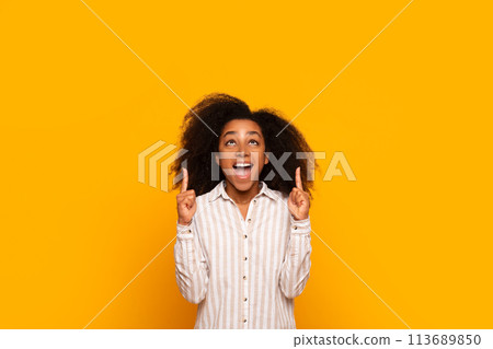 Excited young woman pointing up on yellow Excited young woman pointing up on yellow 113689850