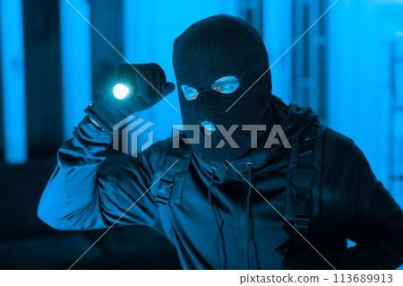 Masked figure with flashlight in blue tone Masked figure with flashlight in blue tone 113689913