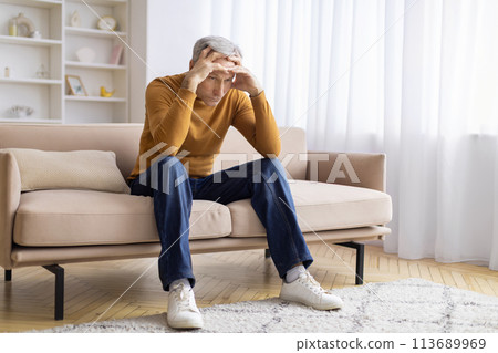 Senior sitting on couch with a hand on head Senior sitting on couch with a hand on head 113689969
