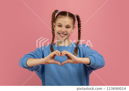 Girl making heart shape with hands on pink backdrop 113690014