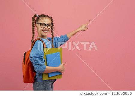 Student girl pointing sideways on pink backdrop Student girl pointing sideways on pink backdrop 113690030