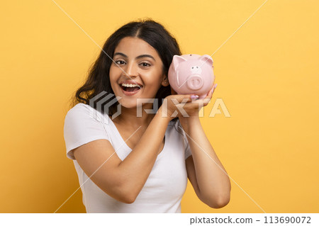 Woman holding a piggy bank with a beaming smile 113690072