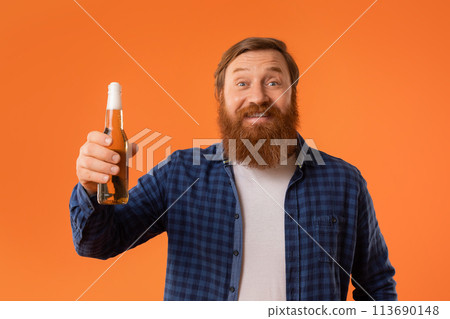redhaired bearded guy raising bottle of beer against orange backdrop 113690148