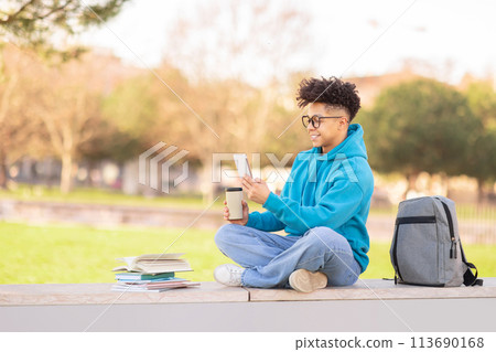 Casual student browsing phone with coffee, studying at park 113690168