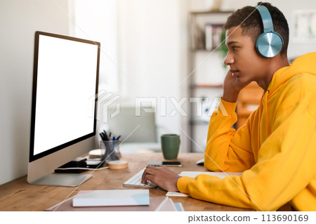 Pensive teen guy at desk with headphones and computer 113690169