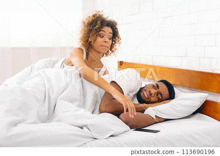 Black woman grabbing phone while her man sleeping 113690196