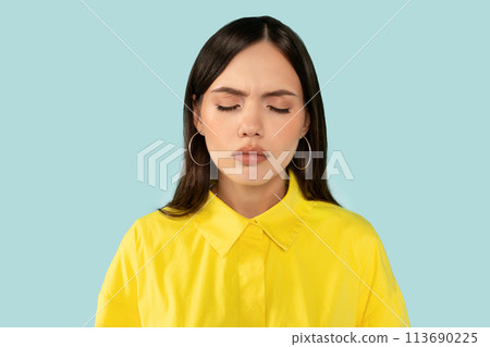 Upset emotional young woman, with eyes closed showing a vulnerable moment of sadness at blue studio background Upset emotional young woman, with eyes closed showing a vulnerable moment of sadness at blue studio background 113690225