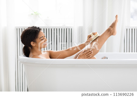 Woman relaxing in bathtub with brush, exfoliating skin Woman relaxing in bathtub with brush, exfoliating skin 113690226